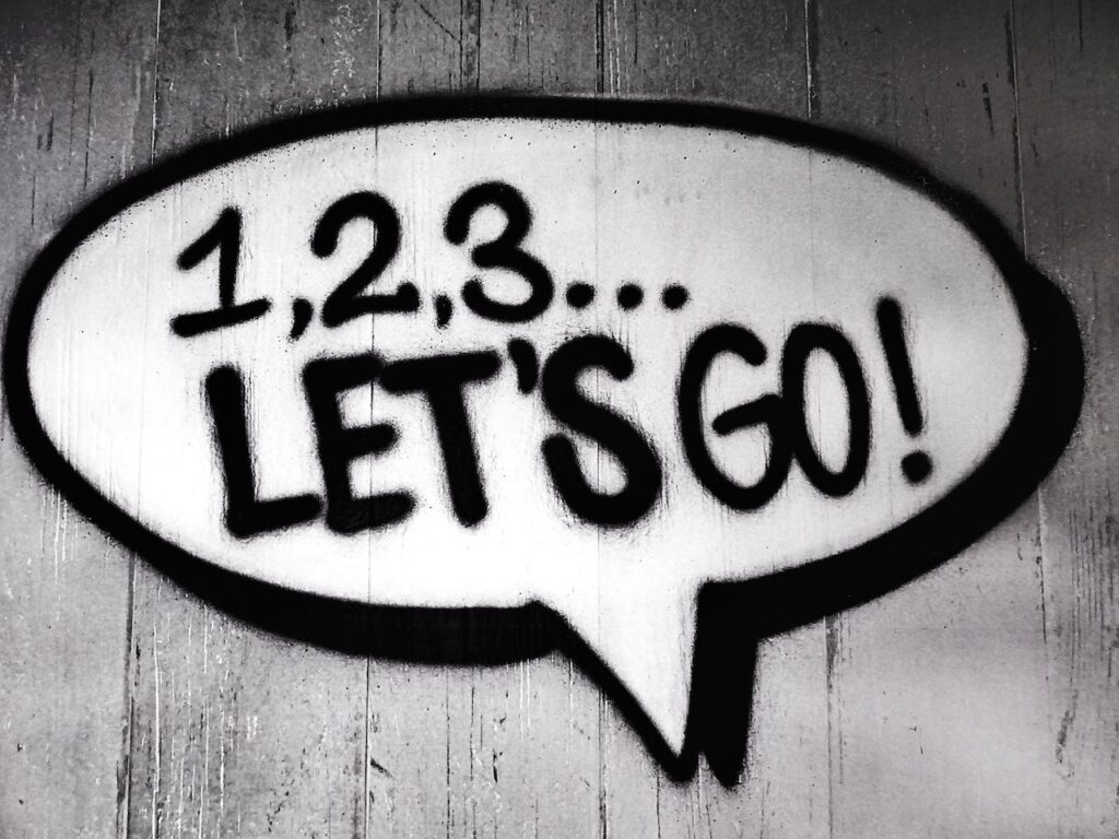 A black and white photo of a speech bubble drawn in graffiti on wood with 1,2,3... LET'S GO! written inside it.