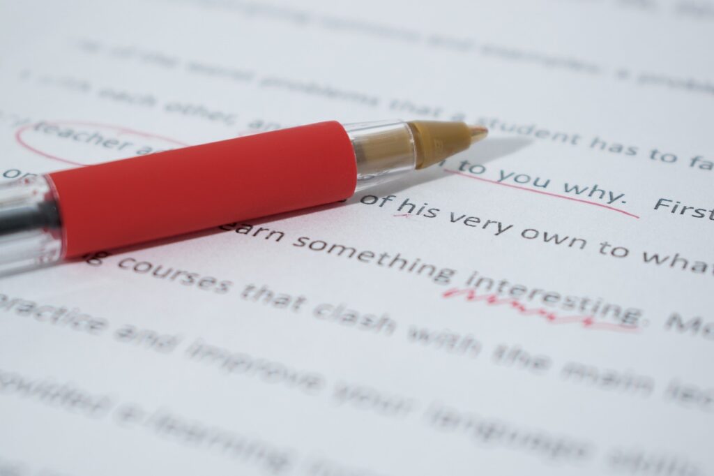 A red biro resting on a page of text where the text has been underlined or had notes added in red ink.