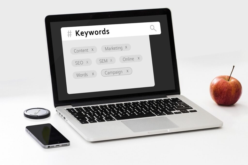 A laptop with the word Keywords in the search bar on the screen and several related words underneath, such as Content, Marketing, SEO and Online